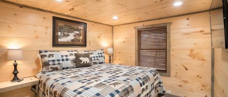 Ein Schlafzimmer mit Holzwänden, einem Bett, Nachttischlampen, einem gerahmten Bild und einem Fenster mit Jalousien.