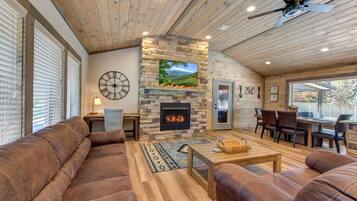 A cozy living room with a stone fireplace, wooden ceiling, and large windows.