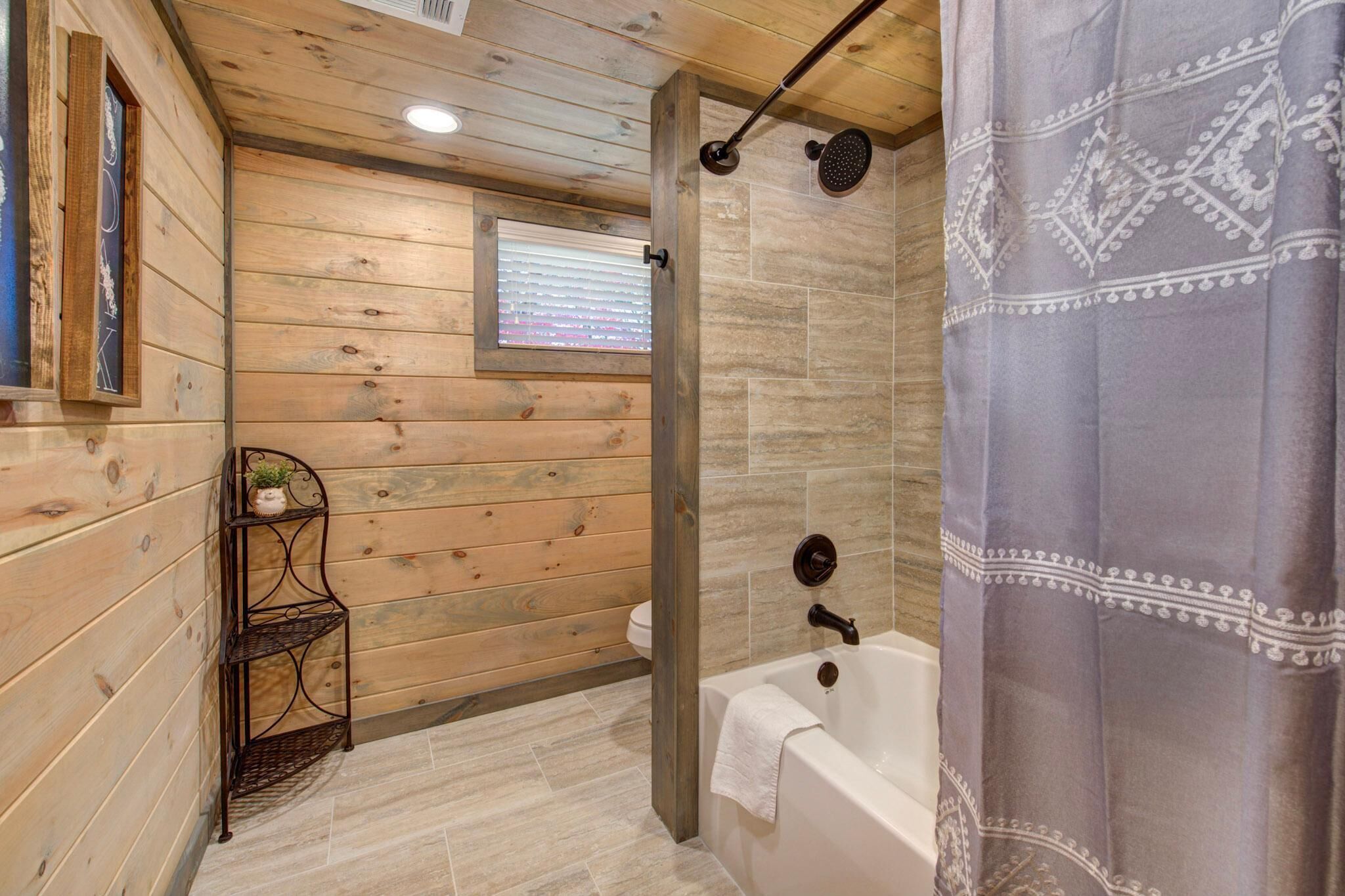 Un baño con paneles de madera, una ducha, un ventanal y una estantería con una planta.