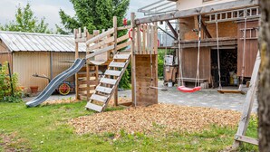 A wooden play structure with a slide and swings, a garage with a metal roof, and a building with a large window. - "Panorama" Maisonette Holiday Apartment with 2 Balconies (Freiamt)