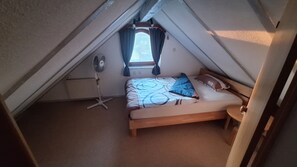 A small, single-bed room with a sloped ceiling, a standing fan, a window with curtains, and a radiator. - "Panorama" Maisonette Apartment with 2 Balconies (Freiamt)