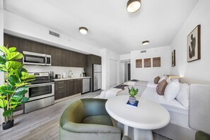 Eine moderne Küche mit Mikrowelle, Herd und Kühlschrank, ein Essbereich mit Tisch und Stühlen sowie ein Wohnbereich mit Sofa und Kissen.