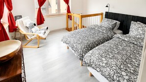 Une chambre à coucher avec un lit, une chaise, une petite table et une fenêtre avec des rideaux rouges.