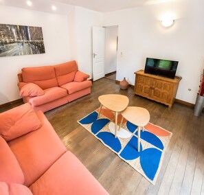 Un salon avec un canapé, une table basse, un téléviseur posé sur un meuble en bois et un tableau accroché au mur.