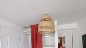 Un couloir avec une porte blanche, un rideau rouge, une lampe en osier, un escalier blanc et un canapé rose.