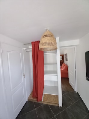 A hallway with a white door, a red curtain, a wicker lamp, a white staircase, and a pink sofa.