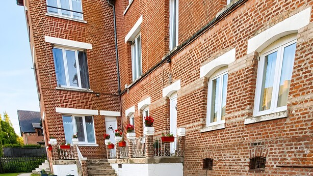 Un immeuble à plusieurs étages, construit en briques, avec un chemin pavé de pierres menant à l’entrée.