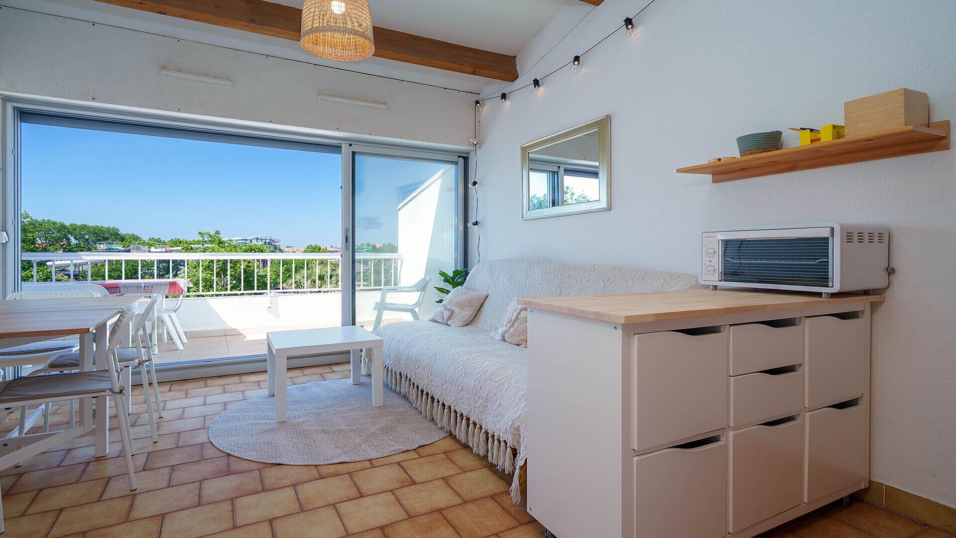Ein modernes Zimmer mit einer Couch, einem Esstisch, Stühlen, einer kleinen Küchenzeile mit Mikrowelle und einem Balkon mit Blick.