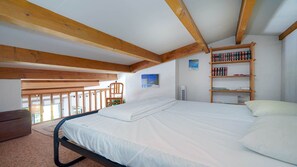 Ein Schlafzimmer mit einem Bett, Holzbalken, einem Bücherregal und einem Fenster.