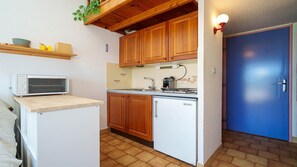 Eine kleine Küche mit Holzausstattung, einem integrierten Backofen, einem kleinen Kühlschrank und einer blauen Tür.