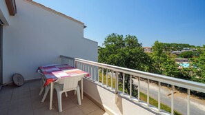 Ein Balkon mit Tisch und Stühlen, Blick auf einen Pool und umgebende Grünflächen.