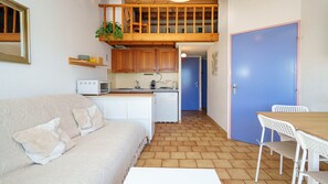 Ein kompakter Wohnraum mit Küchenzeile, einem Essbereich mit Tisch und Stühlen, einer Couch mit Kissen und einer blauen Tür.