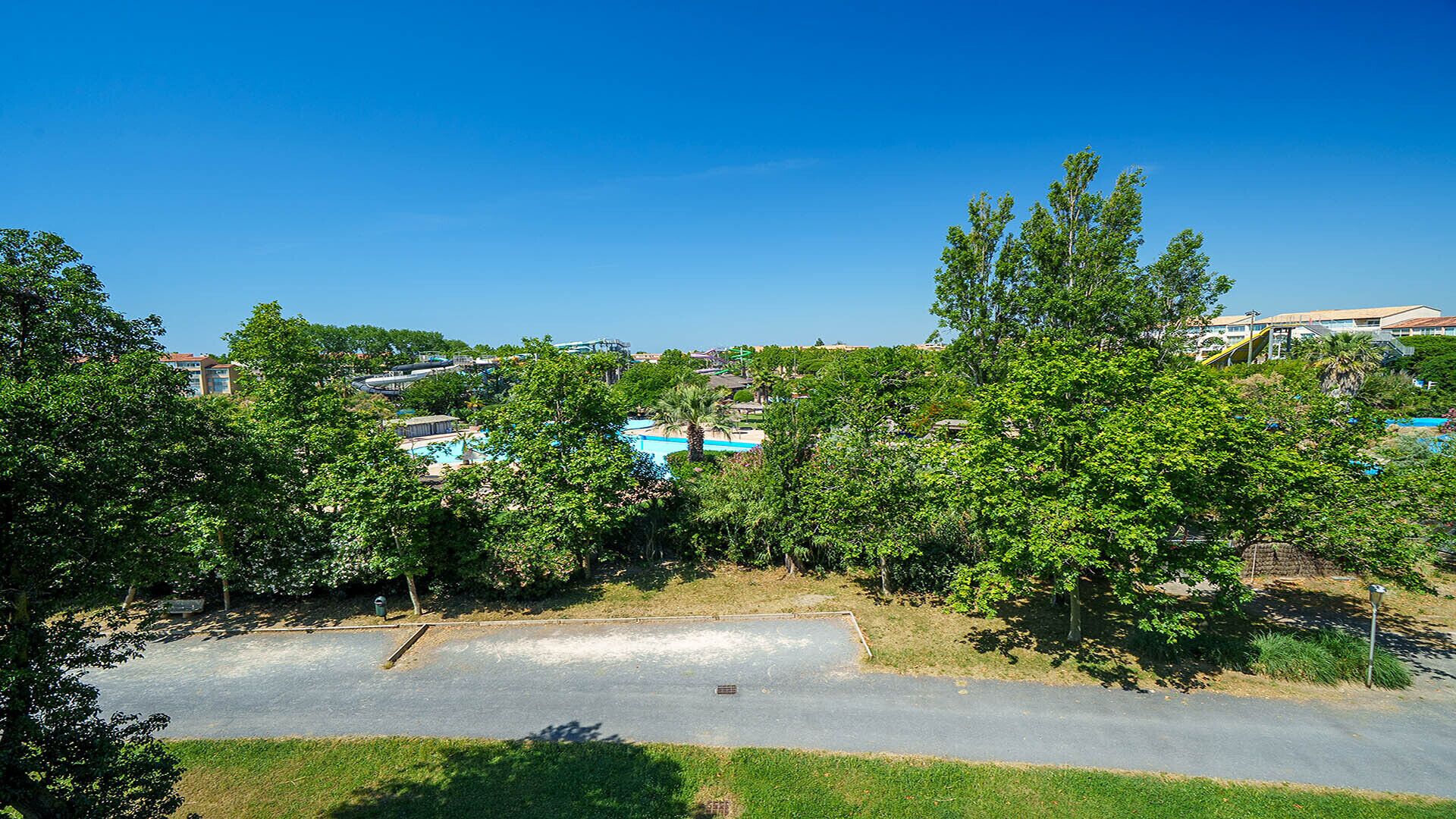 A residential area with a swimming pool, trees, and a road.