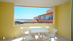 Ein Balkon mit einem weißen Tisch und Stühlen, Blick auf den Strand und ein Gebäude mit einem Ziegeldach.