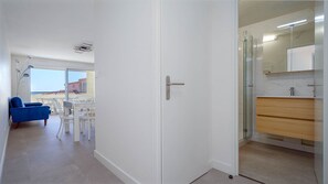 Ein Hotelzimmer mit Balkon, einem Badezimmer mit Glasdusche sowie einem Essbereich mit blauem Stuhl und weißem Tisch.