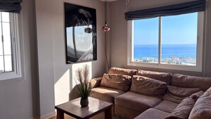 Ein Wohnzimmer mit Sofa, Couchtisch, einem Gemälde und Meerblick.