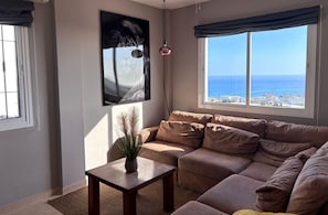 Ein Wohnzimmer mit Sofa, Couchtisch, einem Gemälde und Meerblick.