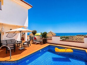 Un área de piscina en la azotea con vista despejada al mar, un espacio de relax con sillas y sombrillas, y un borde decorativo para la piscina.