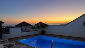Ein Dachpool mit Liegestühlen, einer Topfpflanze und Blick auf den Sonnenuntergang.