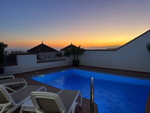 Ein Dachpool mit Liegestühlen, einer Topfpflanze und Blick auf den Sonnenuntergang.