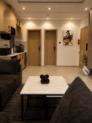 A modern living room with a marble coffee table, a sofa, and a kitchen area with wooden cabinets and a black stove.