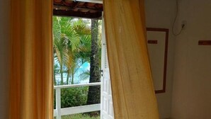 Une chambre d’hôtel avec un lit, des rideaux, un appareil de climatisation et une vue sur des palmiers et une piscine.