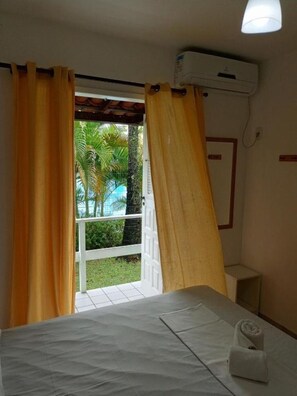 Ein Hotelzimmer mit Bett, Vorhängen, einer Klimaanlage und Blick auf Palmen und einen Pool.