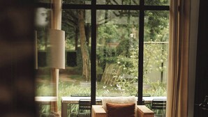 A cozy room with a large window, a wooden chair, a table, and a lamp. - Artist barn near Châtelaudren (Plélo)