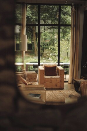 Ein gemütliches Zimmer mit einem großen Fenster, einem Holzsessel, einem Tisch und einer Lampe.