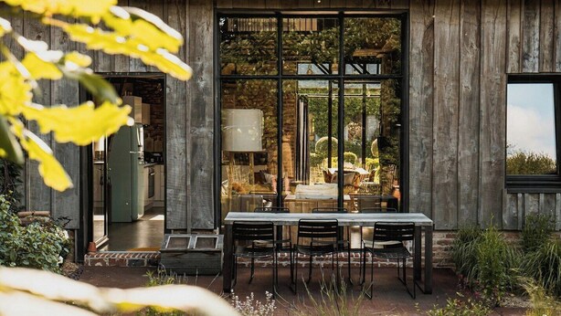 A modern house with a large glass door, a dining area with a table and chairs, and a view of the garden. - Artist barn near Châtelaudren (Plélo)