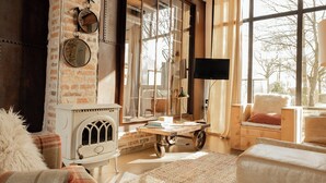 A cozy living room with a fireplace, large windows, and rustic decor. - Artist barn near Châtelaudren (Plélo)