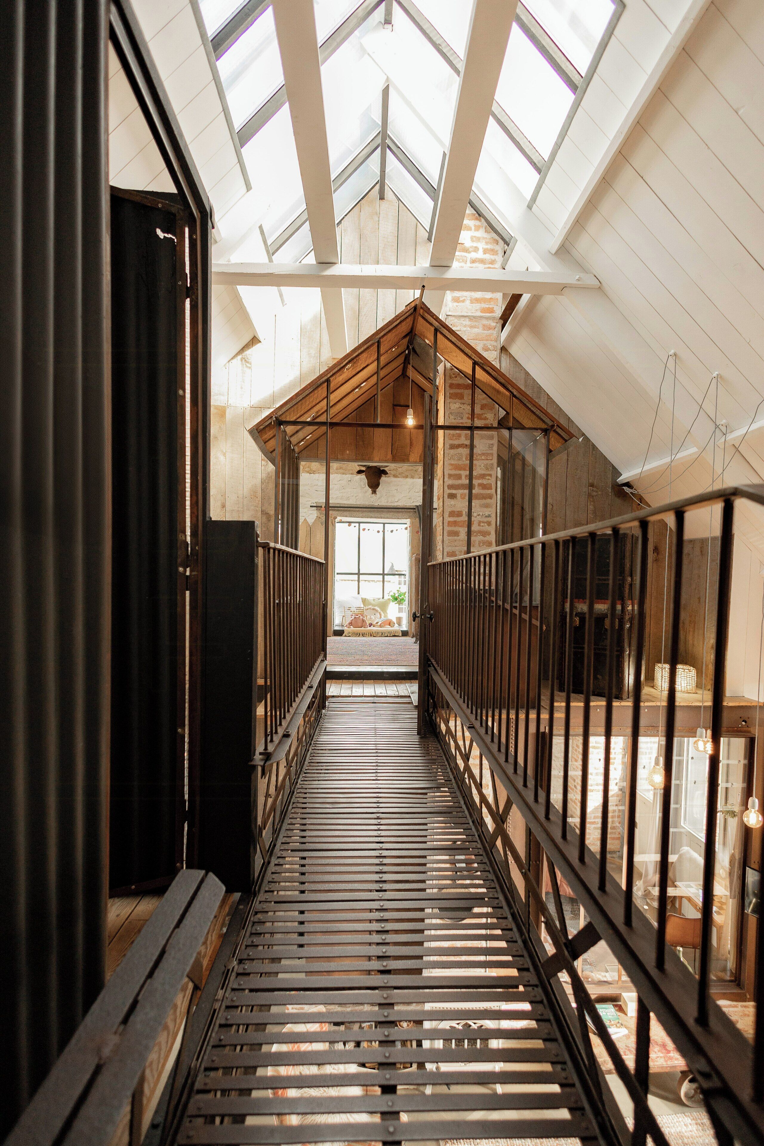 A corridor with a skylight, wooden beams, and a metal railing.