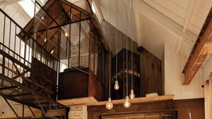 A loft-style room with a high ceiling, exposed beams, and a loft area with a wooden staircase. - Artist barn near Châtelaudren (Plélo)