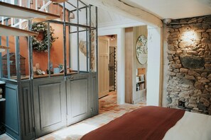 Ein Zimmer mit einem Bett, einer Steinwand, einer Holztreppe und einer Küchenzeile mit Schränken und einem hängenden Kranz.