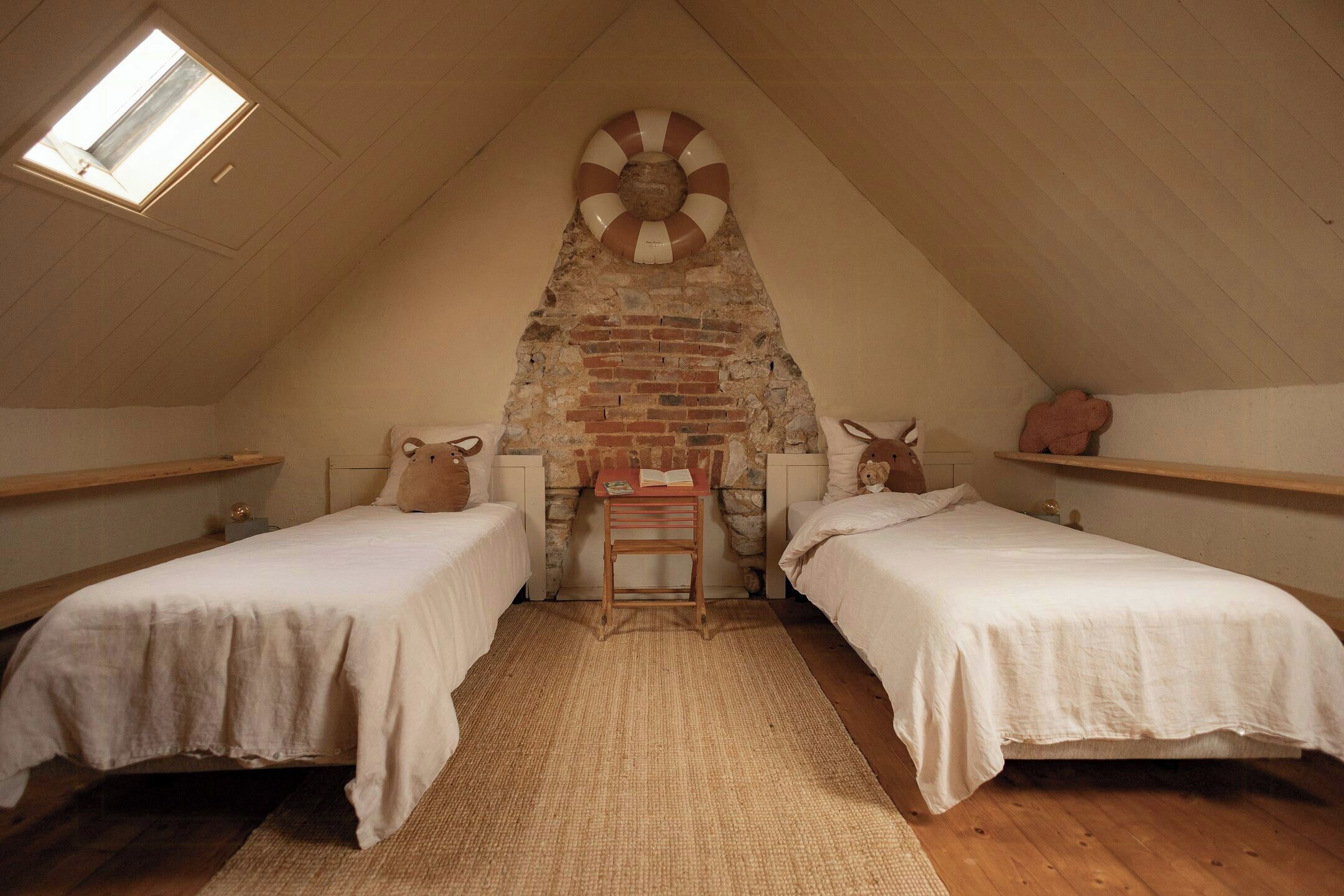 A room with two beds, a small table, and a brick wall.