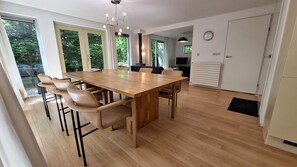 Ett modernt matområde med ett träbord och stolar, stora fönster och ett köksutrymme som är synligt.