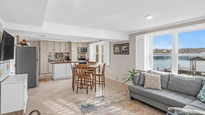 A modern kitchen with a dining area, a gray sofa, and a view of a body of water.