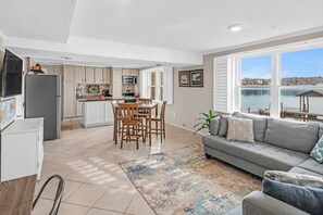 A modern kitchen with a dining area, a gray sofa, and a view of a body of water.