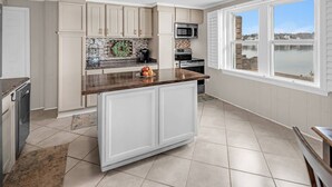 A kitchen with white cabinets, a granite countertop, a microwave, and a view of a lake through large windows.