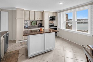A kitchen with white cabinets, a granite countertop, a microwave, and a view of a lake through large windows.