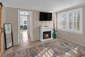 A living room with a fireplace, a TV mounted on the wall, and a view through the window.