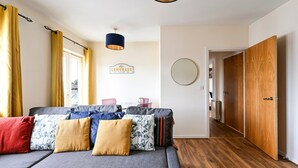 Een moderne woonkamer met een bank, kussens, een hanglamp, een bordje met de tekst 'LEMONADE' en een houten deur.