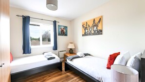 Een kamer met twee bedden, een raam met gordijnen, een lamp en kunst aan de muur.