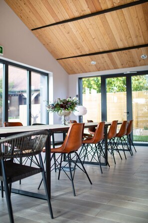 Un comedor moderno con techo de madera, ventanas amplias y una mesa con sillas.