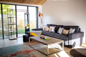 A modern living room with a grey sofa, a coffee table, and a large window with a view of a garden.
