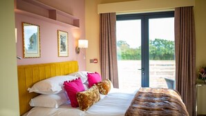 A hotel room with a bed, a window with curtains, a wall-mounted light, and framed pictures.