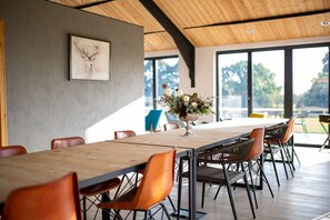 A spacious dining area with a long wooden table, multiple chairs, and a large window offering a view of the outdoors.