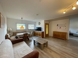 A living room with a sofa, a dining table, a TV, wooden cabinets, and a clock on the wall.