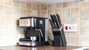 Uma máquina de café com espumador de leite e moedor, um porta-facas com facas, e uma tomada em uma bancada de cozinha.