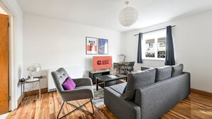 Uma sala de estar moderna com um sofá cinzento, uma poltrona cinza, uma mesinha, uma televisão e uma janela com cortinas.